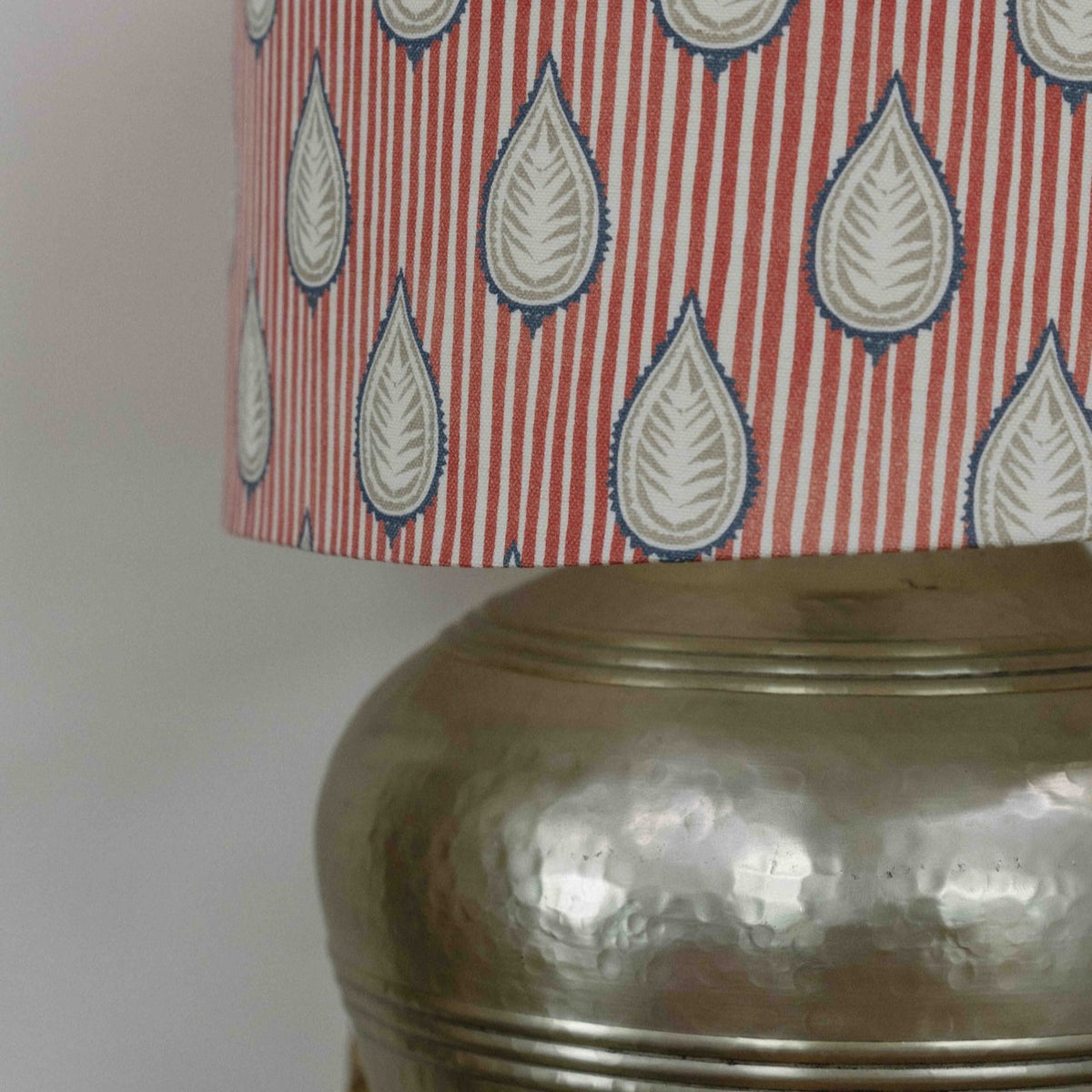 Close-up of a table lamp featuring a red and white striped fabric shade with a blue and gray teardrop pattern, mounted on a hammered metallic gold base.