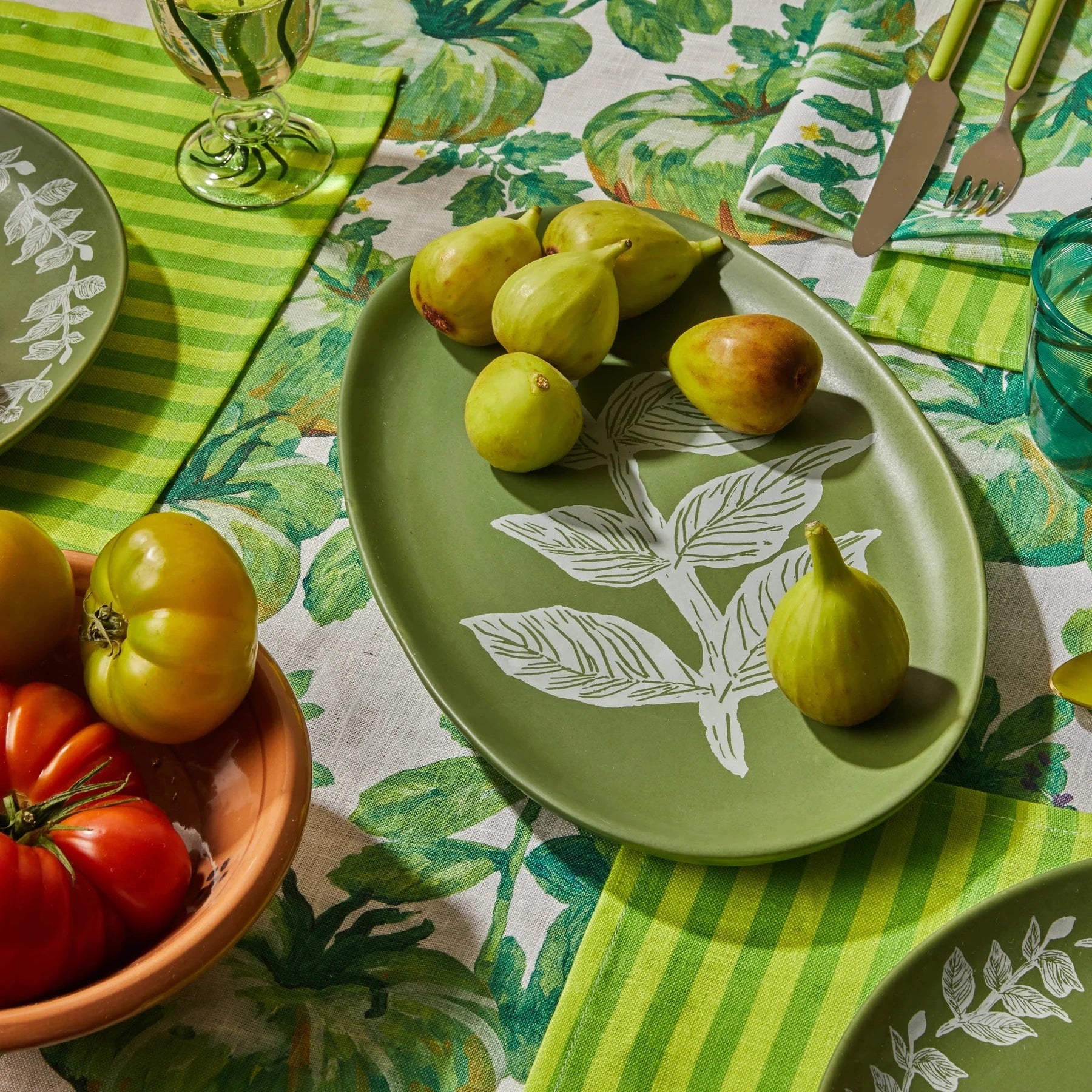 Green table setting with leaf-patterned plates and napkins on a matching tablecloth.