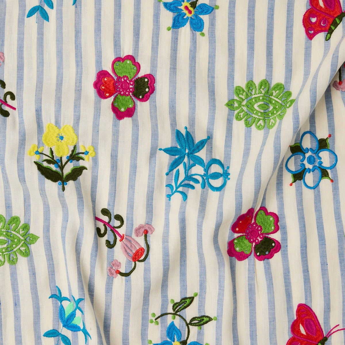 A close-up of a fabric surface with vertical light blue and white stripes, decorated with colorful embroidered floral and butterfly motifs in pink, blue, green, yellow, and red.