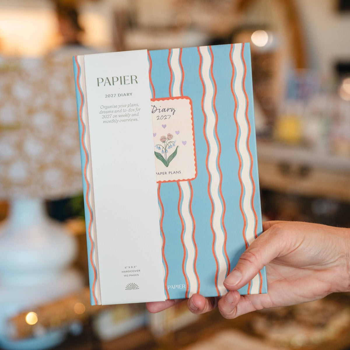 Papier 2027 hardcover weekly diary featuring a blue cover with coral and cream wavy stripes, floral illustration and Paper Plans design.