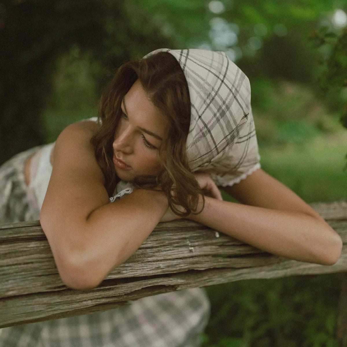 Woman resting her head on a wooden surface with a blurred green background