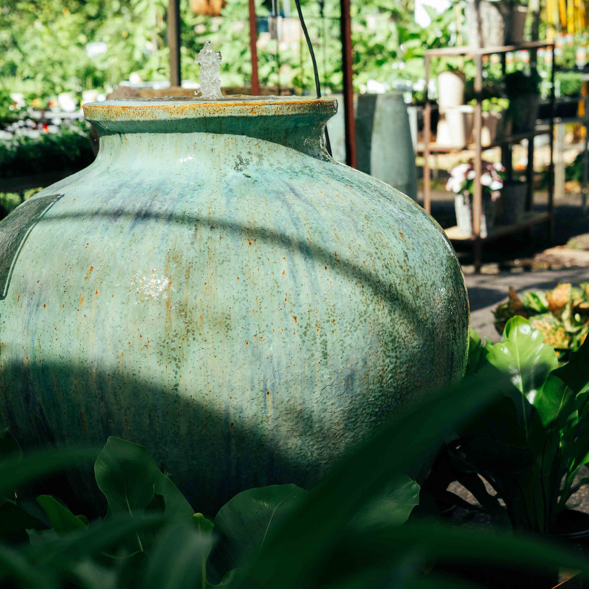 Large Shangri La glazed ceramic garden fountain with matching base and bubbling water feature surrounded by lush tropical plants. Brisbane Gardens