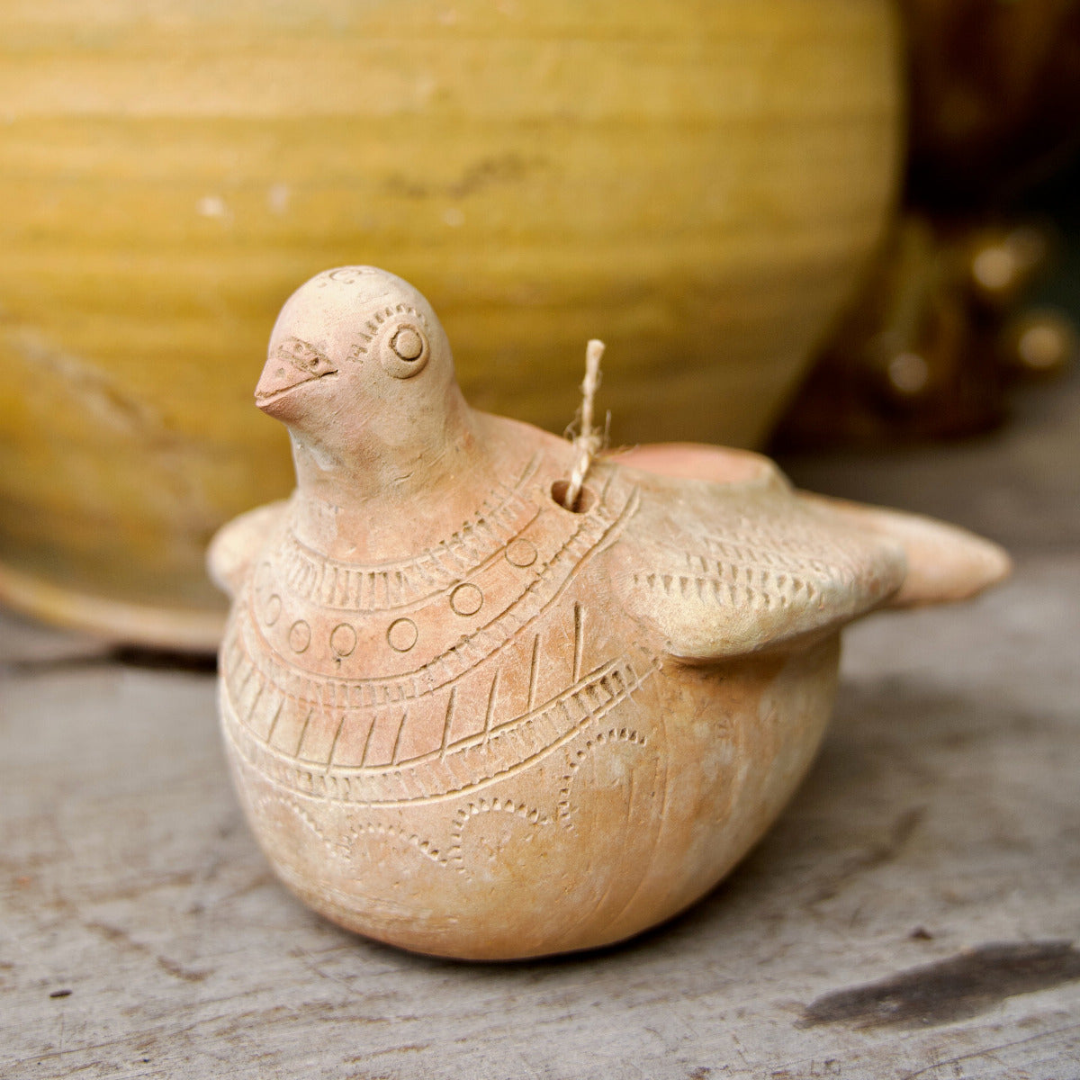 Decorative terracotta bird with intricate patterns on a wooden surface with a blurred natural background
