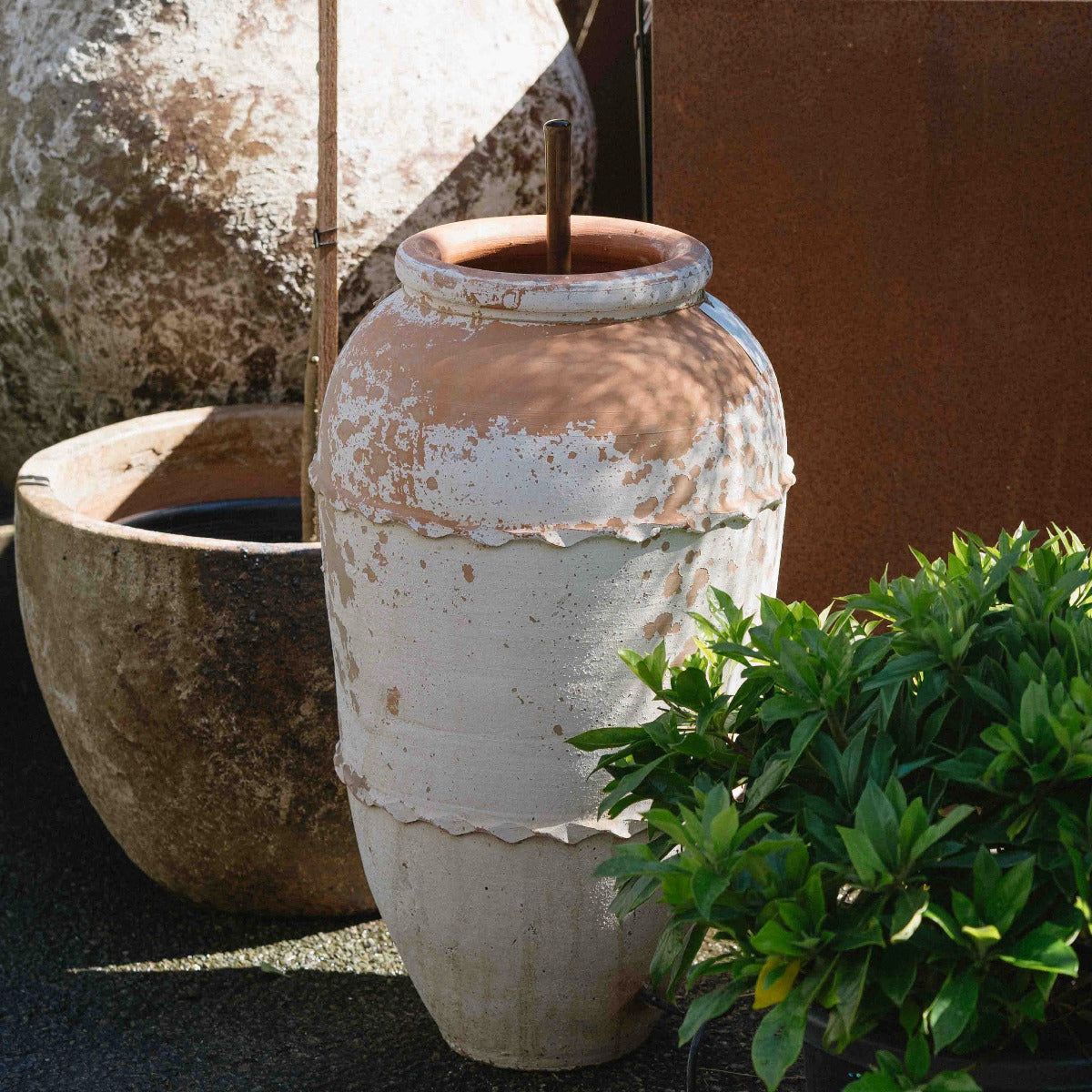 Weathered Turkish Odemis pot fountain with a simple copper water spout surrounded by garden plants.