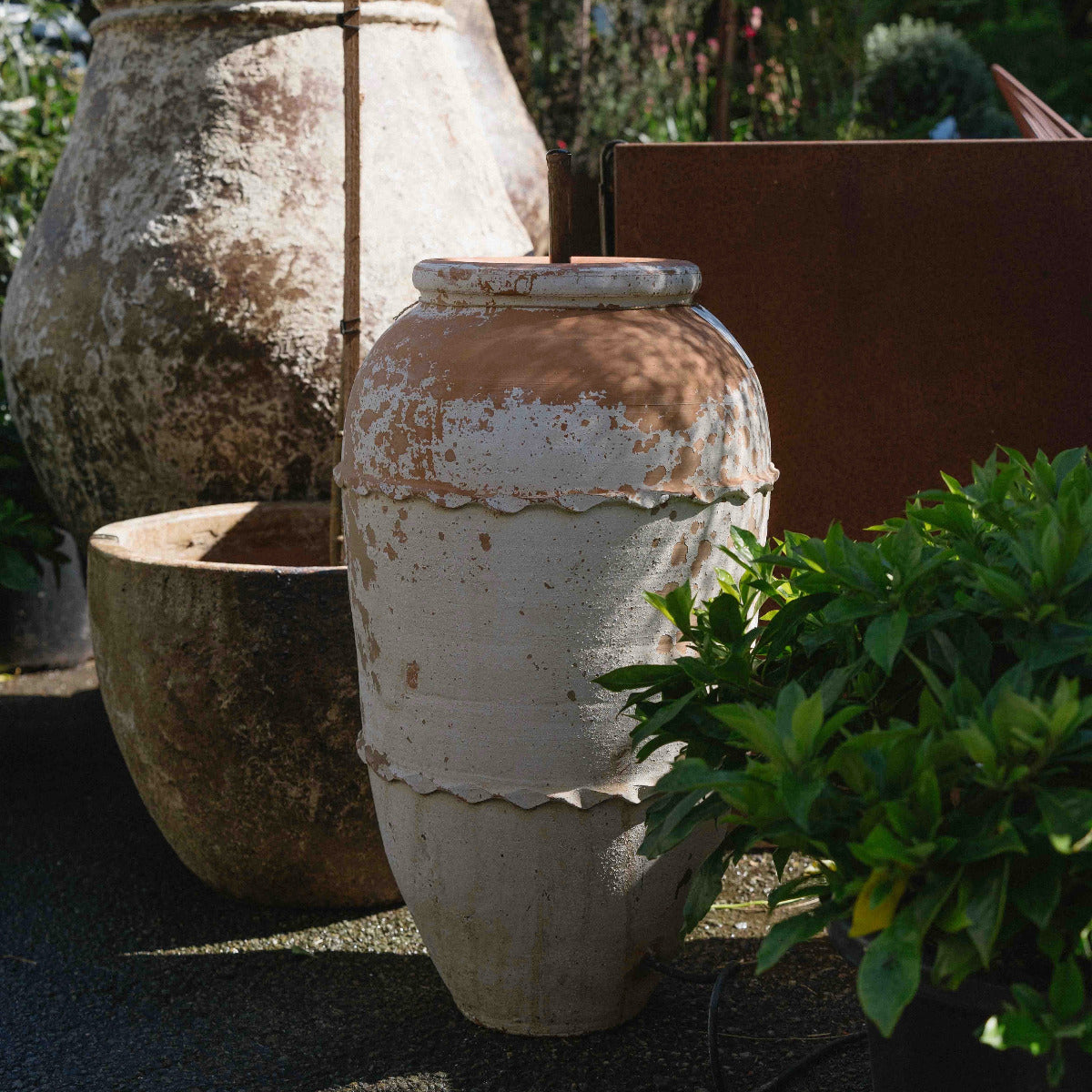 Weathered Turkish Odemis pot fountain with a simple copper water spout surrounded by garden plants.